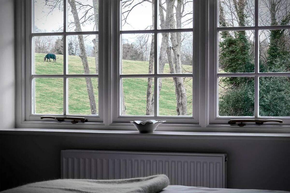 Quarto com uma janela grande que dá para um campo gramado e árvores.