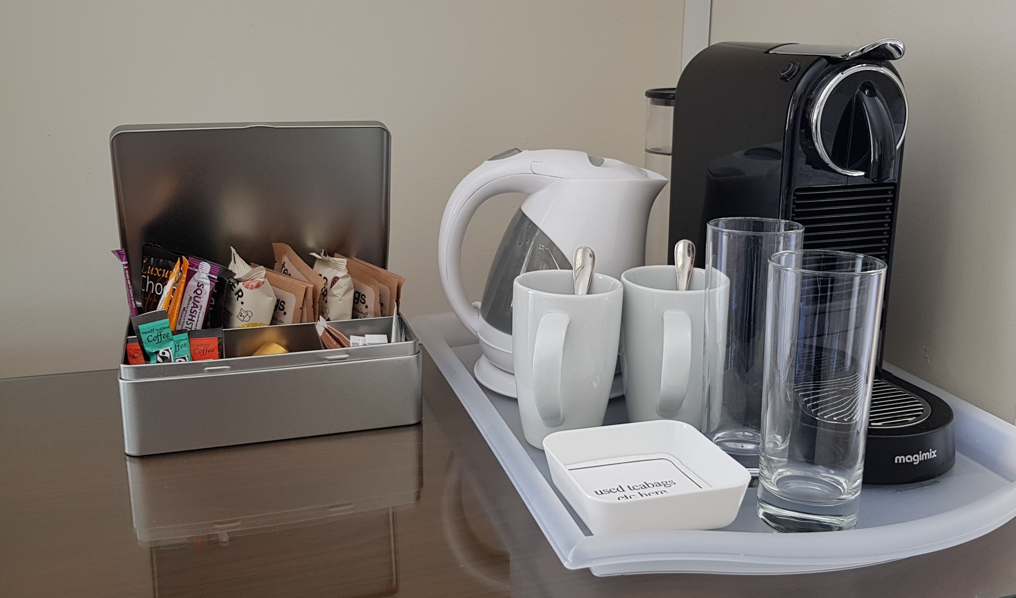 Una estación de café con cafetera, tazas y una bandeja con un portal cápsulas de café y un vaso.