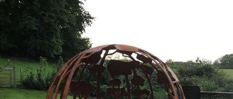 Una escultura metálica esférica con siluetas de animales, ubicada sobre un terreno de grava en un parque.