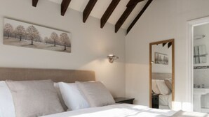 A bedroom with a bed, a nightstand, a wall-mounted light, and a painting of trees. - Hurtwood Hotel (Guildford)