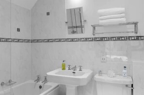 A bathroom with a bathtub, a sink, and a toilet. There is a towel rack with folded towels above the sink. - Hurtwood Hotel (Guildford)