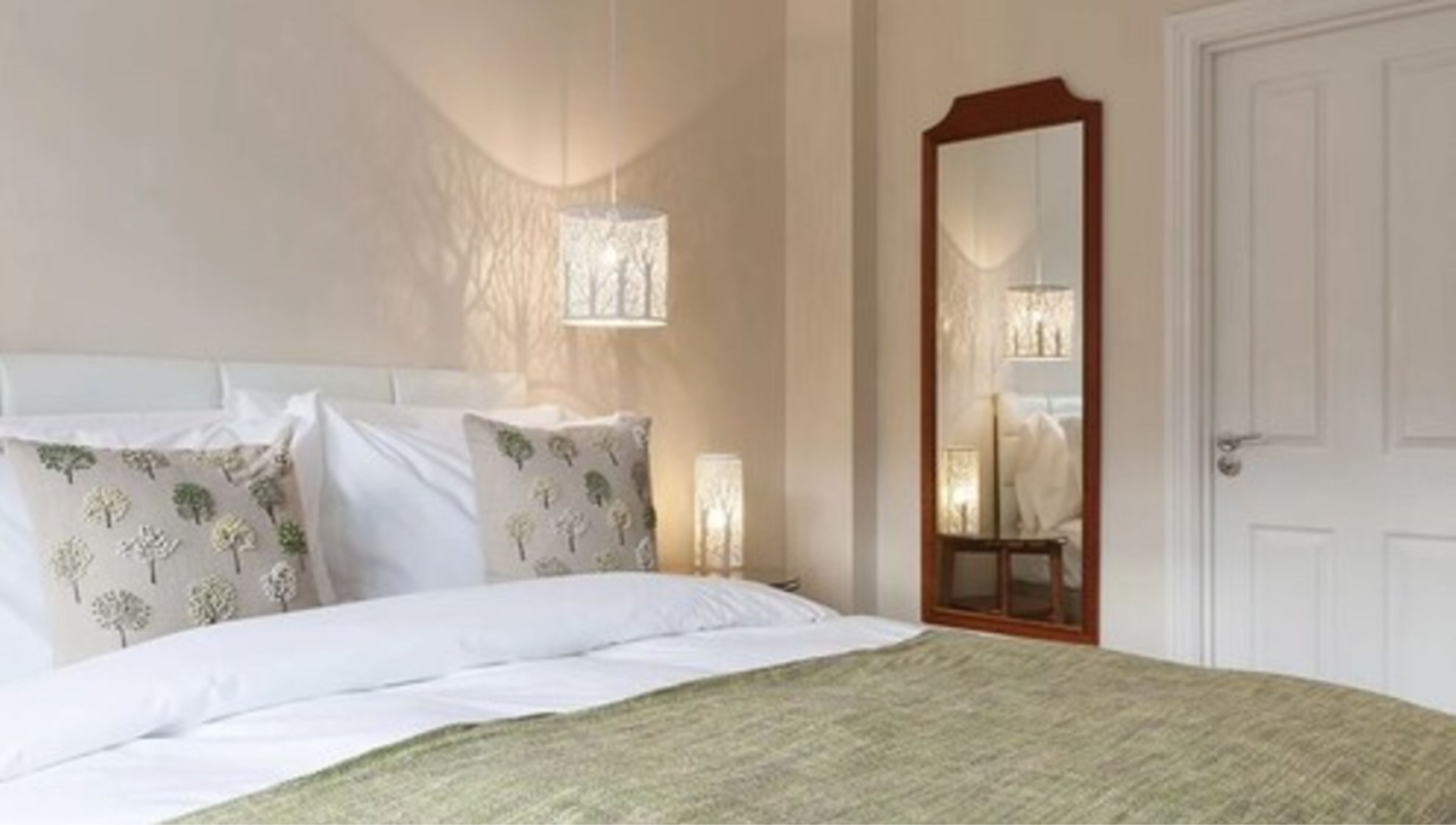 Un lit bien fait, avec du linge de lit blanc et un plaid vert, une table de chevet avec une lampe, et un grand miroir accroché au mur.