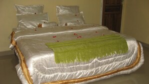 A neatly made bed with a satin cover, a green throw, and rose petals scattered across the bed. - Richland Lodges Kalomo (Livingstone)