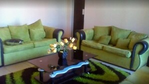 A living room with two green sofas, a coffee table with a vase of yellow flowers, and a patterned rug. - Richland Lodges Kalomo (Livingstone)