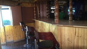 A wooden interior with a bar area, two stools, and a window. - Richland Lodges Kalomo (Livingstone)