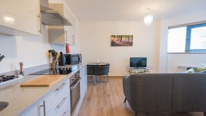 A modern kitchen with a dining area, a flat-screen TV, and a grey sofa. - Hamilton Grace - The Quadrant (Swindon)