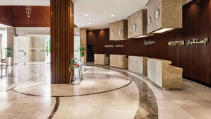 Una moderna zona de recepción con suelo de mármol curvo, paneles de madera y una recepción con relojes.
