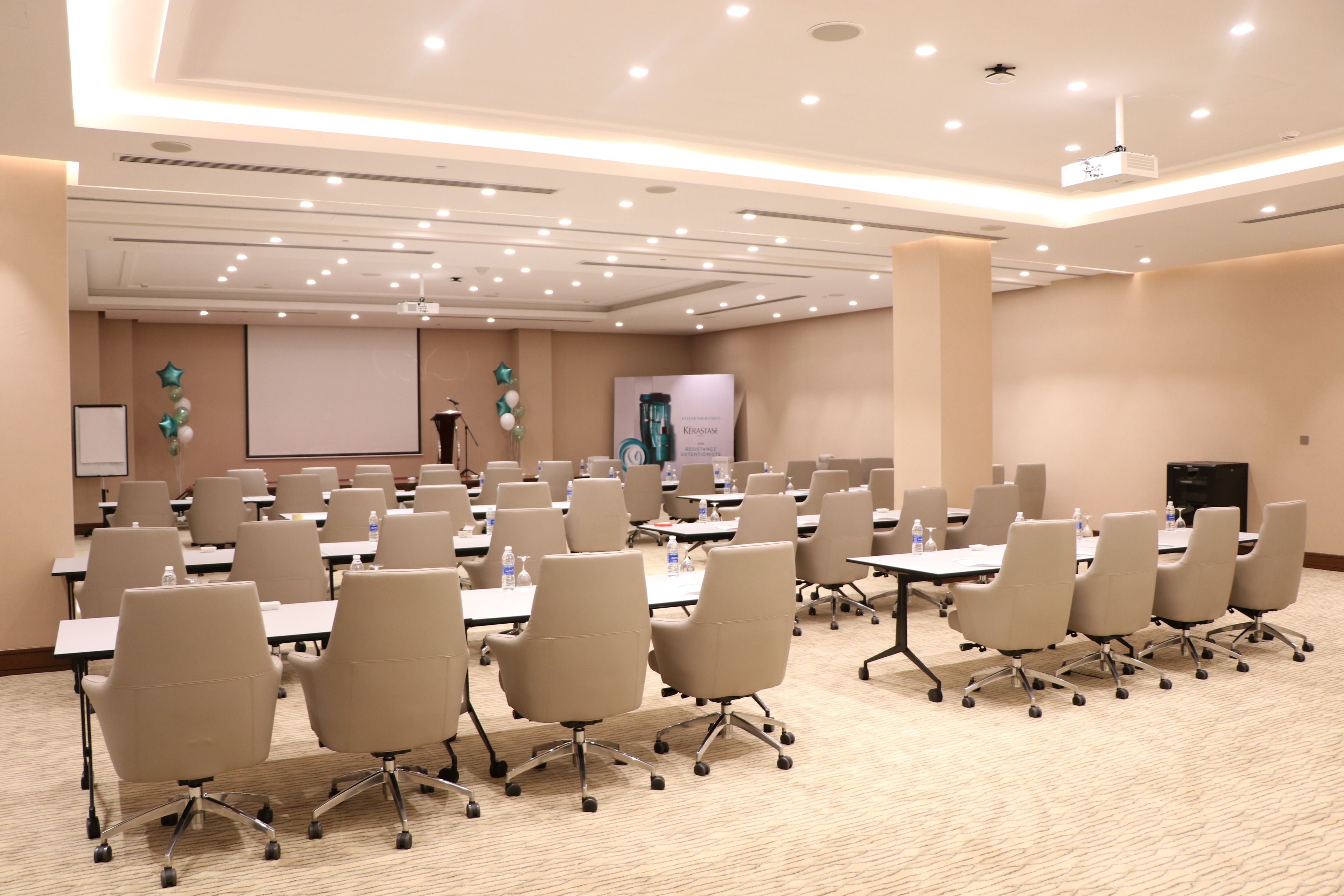 A conference room with multiple tables and chairs, a projector screen, and a presentation board.