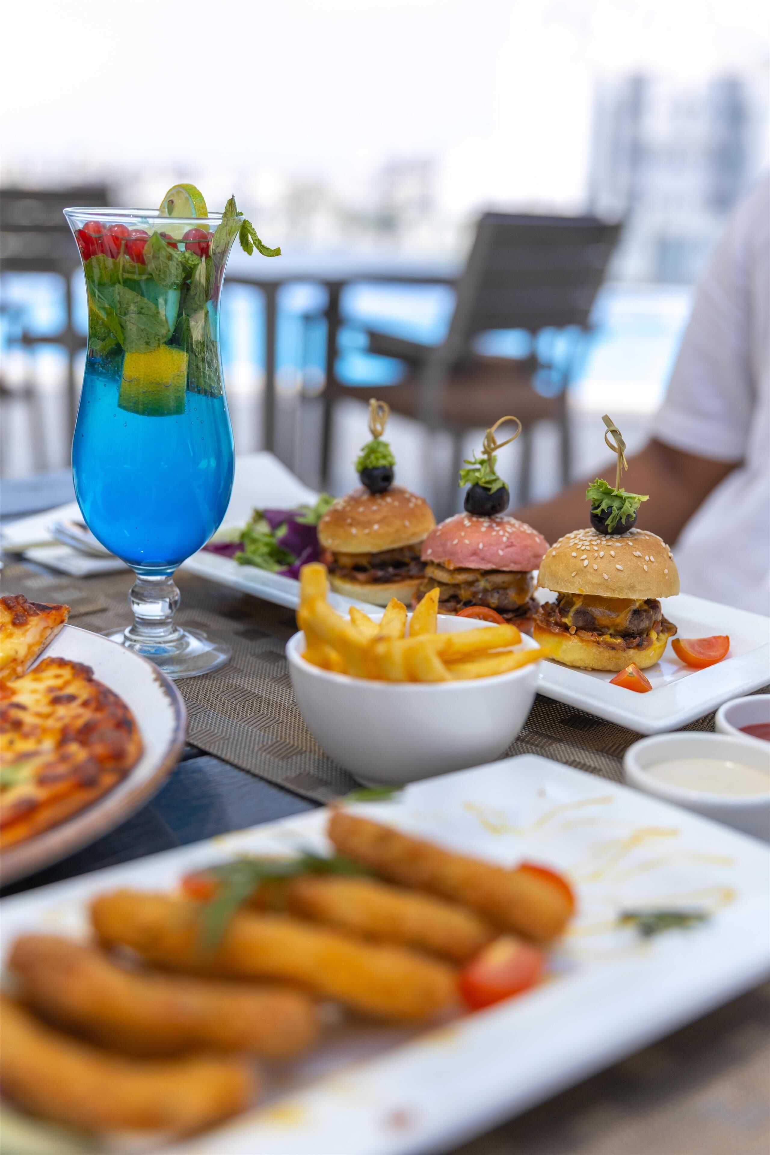 A table with various dishes including burgers, fries, and a blue cocktail.