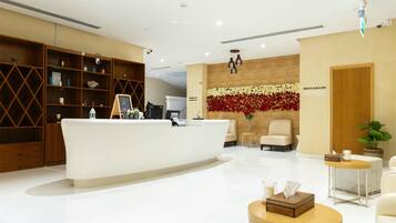 Un área de recepción con un mostrador blanco, estanterías de madera, una pared decorada con flores rojas y blancas, y un letrero que dice "HEALTH CLUB & SPA".