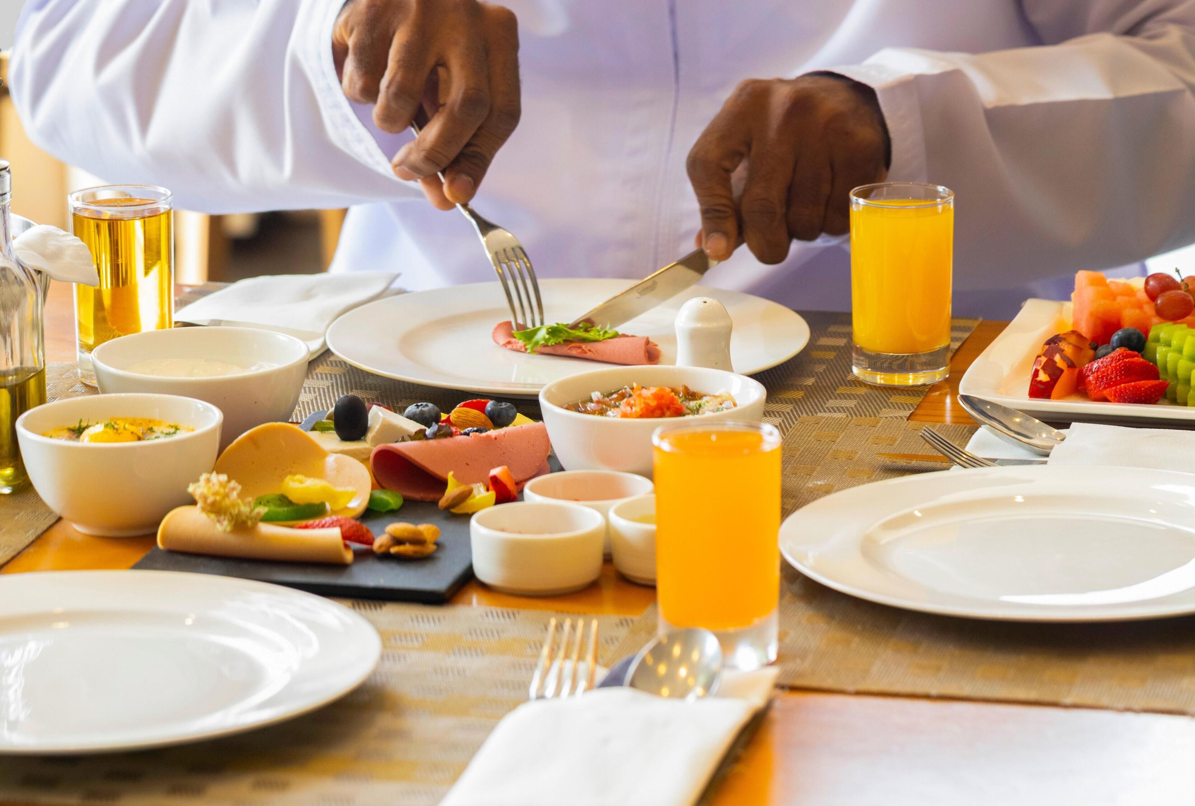 Une table dressée pour le petit-déjeuner, avec une variété de plats, notamment un hot-dog, des fruits et un verre de jus d’orange.