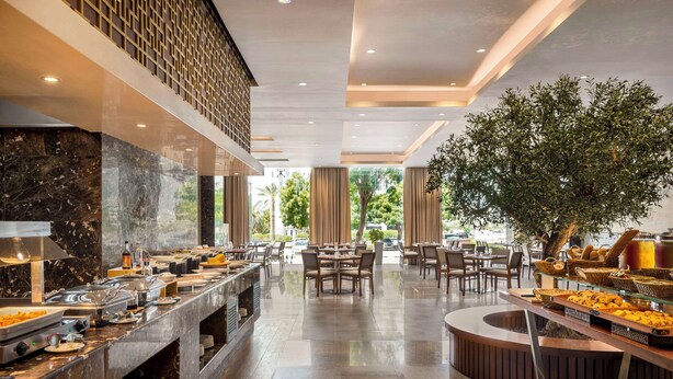 Zona de buffet con mostradores de mármol, varias estaciones de comida y disposición de mesas.