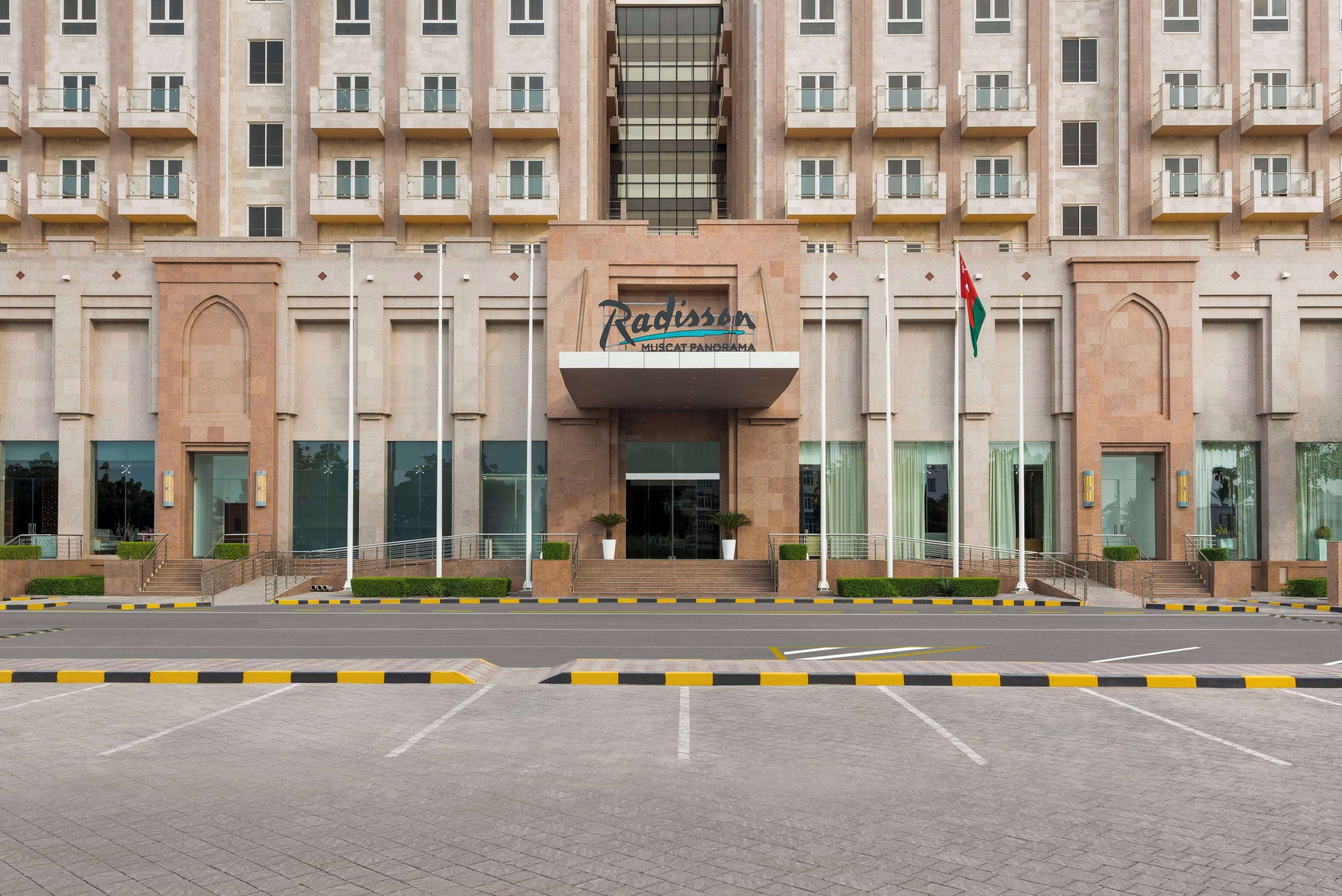 Ein großes, mehrgeschossiges Gebäude mit einem markanten Eingang, auf dem "Radisson Muscat Panorama" steht.