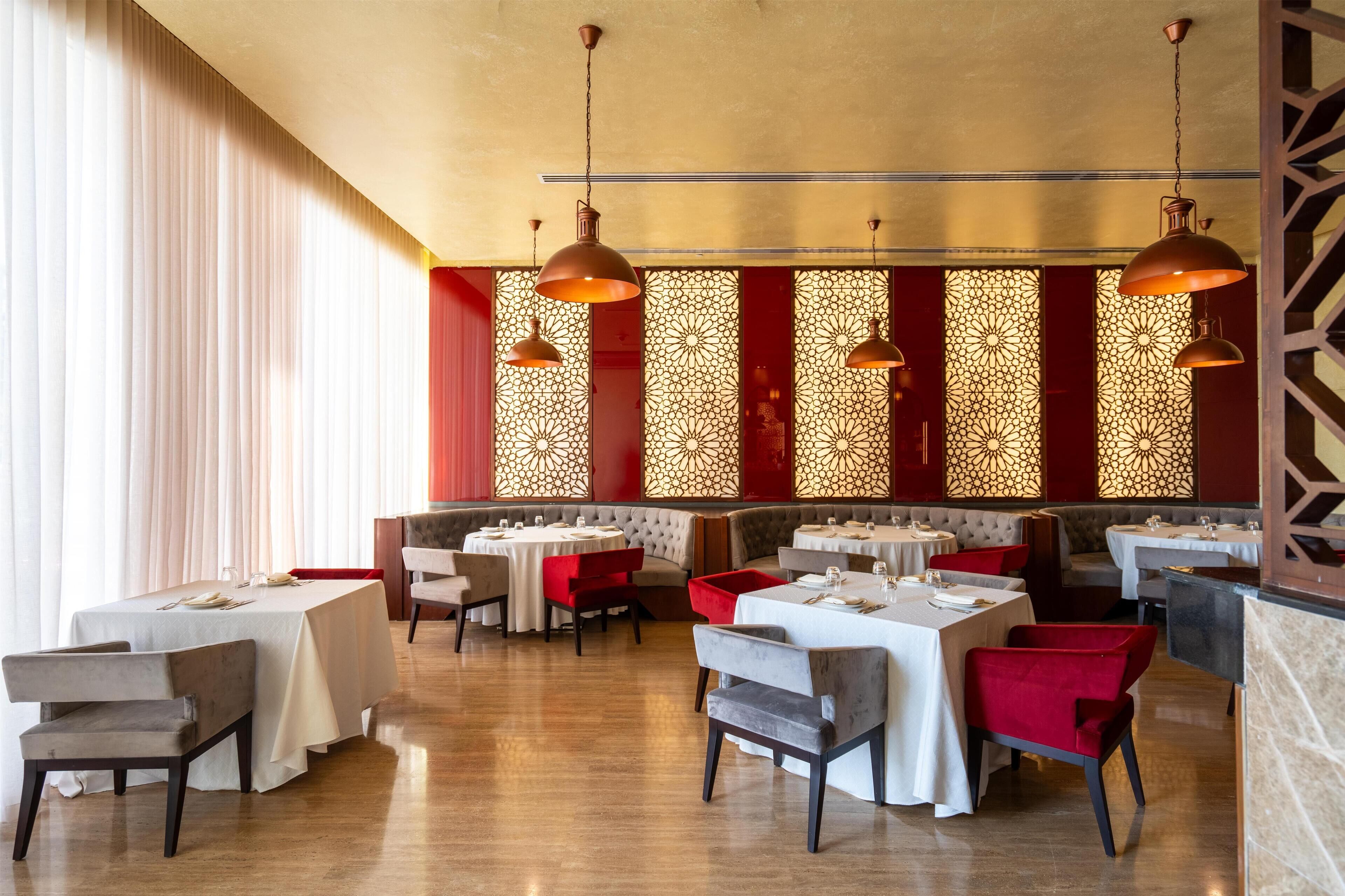 A restaurant with multiple tables and booths, featuring a modern interior with patterned wall decorations and pendant lighting.