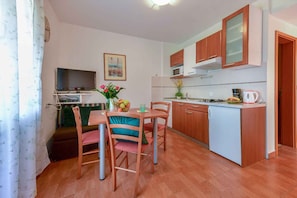 Una cocina compacta con armarios de madera, una mesa de comedor con sillas, un televisor y una pequeña isla con microondas.