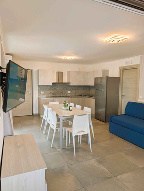 Eine moderne Küche mit weißen Schränken, einer Arbeitsplatte aus Granit, einem Edelstahlkühlschrank und einem Essbereich mit Tisch und Stühlen.