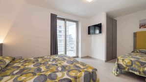 Habitación de hotel con dos camas, televisión y balcón con vistas a la ciudad.