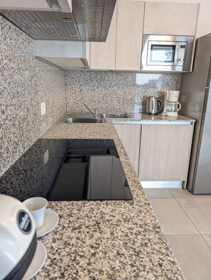 Eine Küche mit Granit Arbeitsplatten, einem eingebauten Ofen, einer Mikrowelle, einer Kaffeemaschine und einem Edelstahl-Kühlschrank.