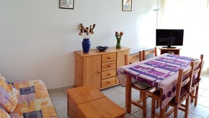 Una sala de estar acogedora con un sofá, un aparador de madera, una mesa de comedor con sillas y un televisor.