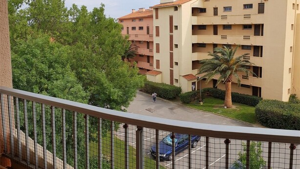 Un edificio residencial de varios pisos con balcones, zona de estacionamiento y vegetación circundante.