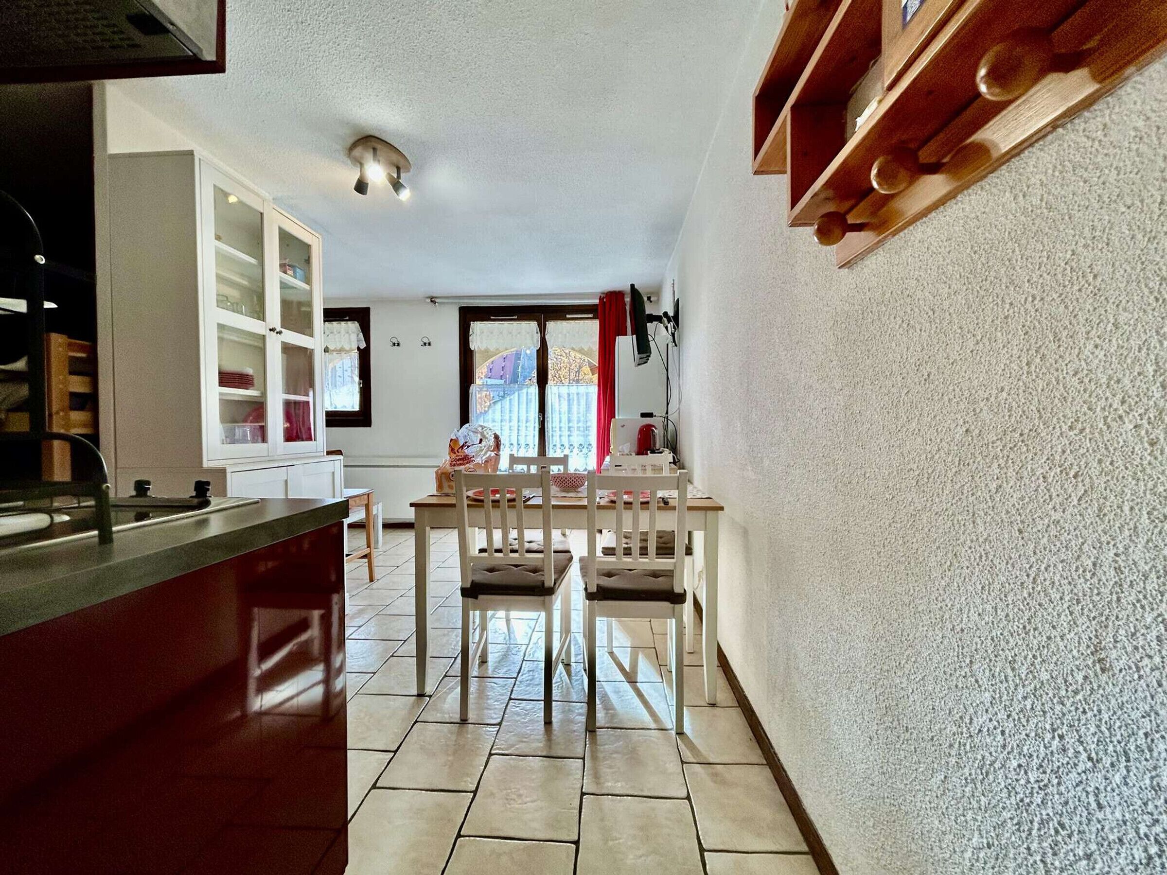 A kitchen with a dining area, a window with curtains, and a ceiling light fixture.