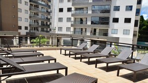 Une terrasse sur le toit, dotée de plusieurs chaises longues et de tables, et entourée d’une rambarde en verre.