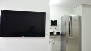 Une cuisine équipée d’un grand téléviseur à écran plat fixé au mur, d’un réfrigérateur en acier inoxydable et d’un four à micro-ondes.