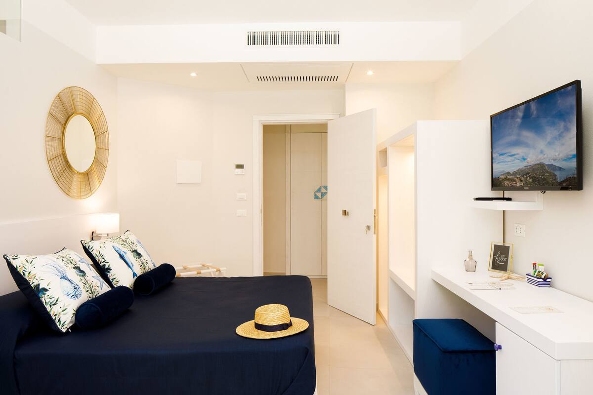 Een moderne hotelkamer met een bed, bureau, televisie en een deur naar een andere kamer.