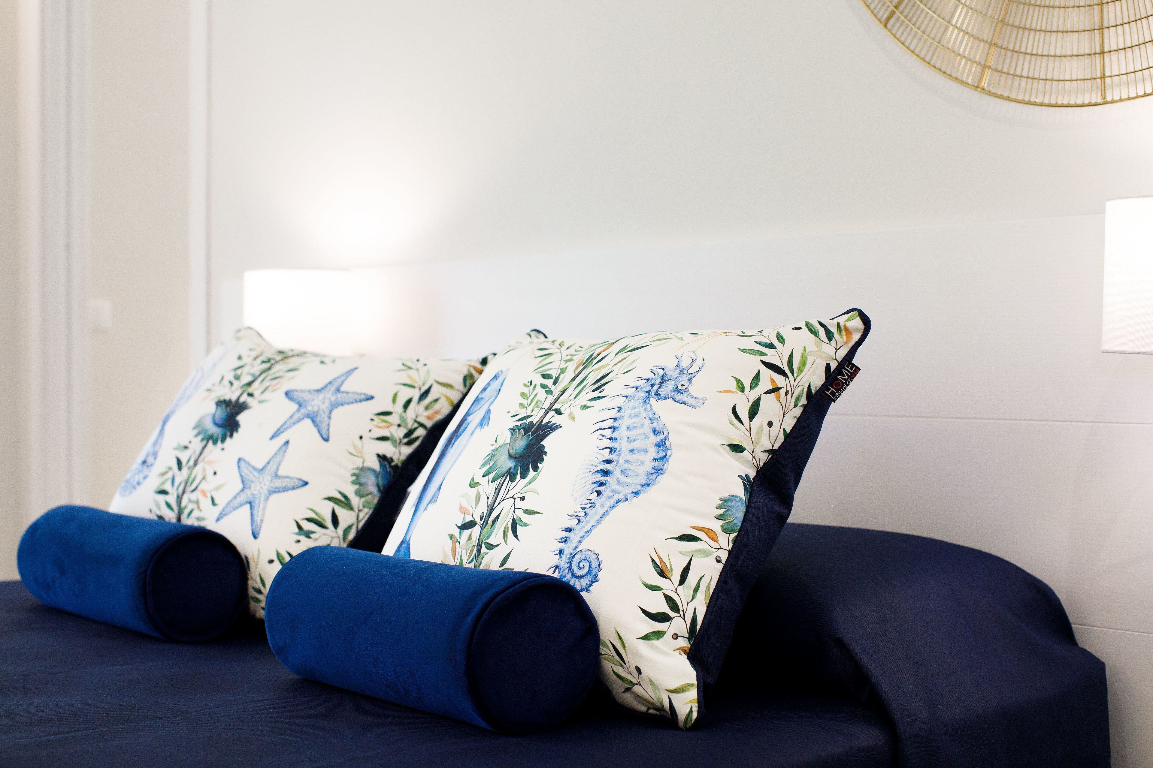 A bed with two decorative pillows featuring a seahorse and starfish design, and two rolled-up blue pillows.