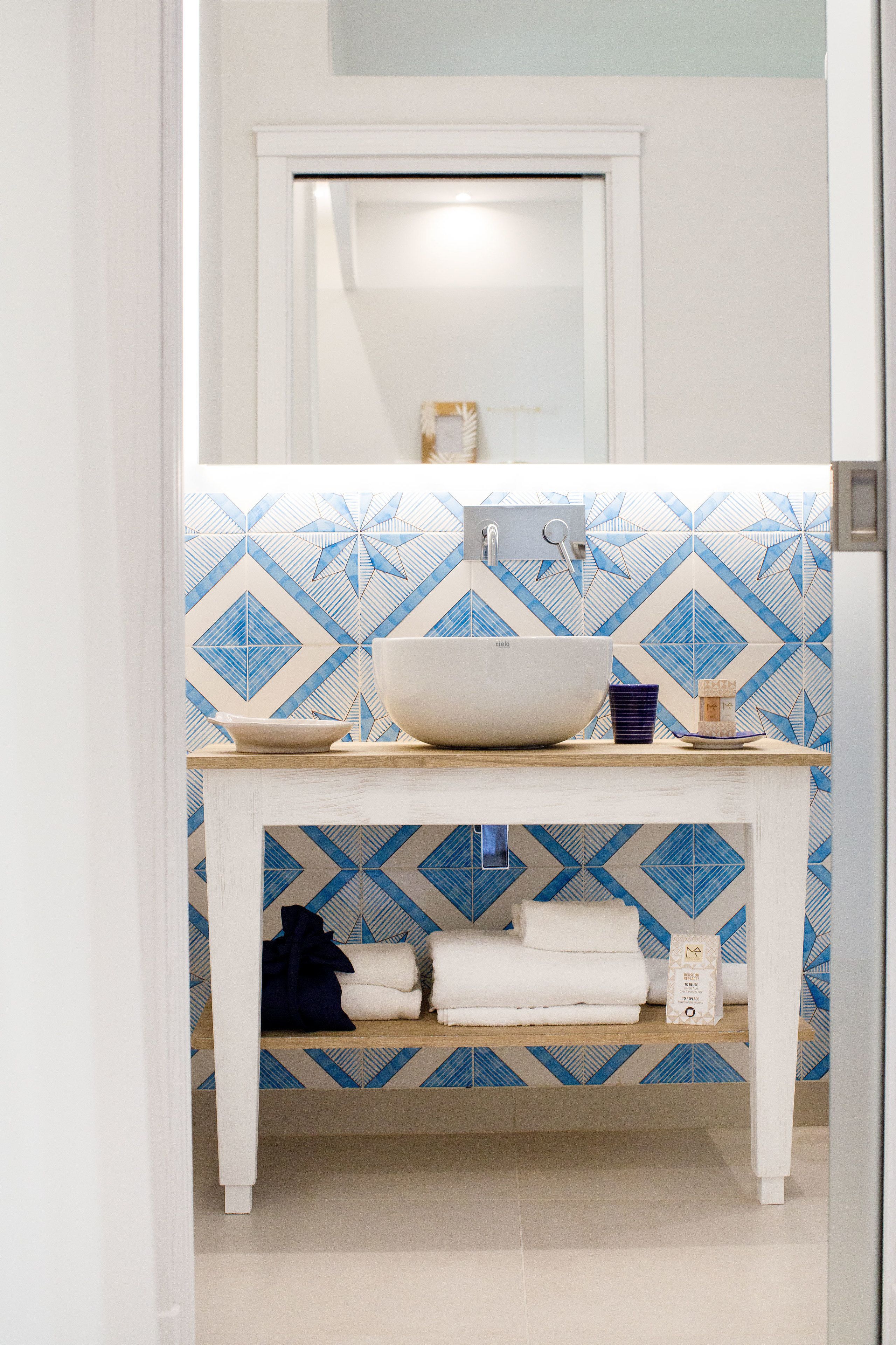 A bathroom with a white sink, blue patterned tiles, and a wooden vanity.