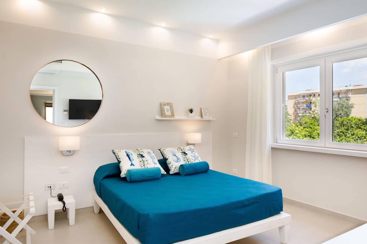 Een slaapkamer met een bed, nachtkastje, lamp en een ronde spiegel aan de muur.