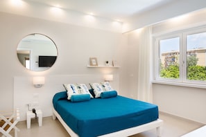 A bedroom with a bed, bedside table, lamp, and a round mirror on the wall. - Melrose Sorrento (Sorrento)