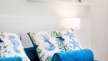 Ein Schlafzimmer mit einem Bett, zwei Kissen mit Seepferdchen- und Sternfisch-Motiv, einer blauen Decke und einer weißen Wand mit einem Regal über dem Bett.
