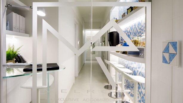 Una cocina moderna con armarios blancos, encimera de cristal y un salpicadero con estampado azul.