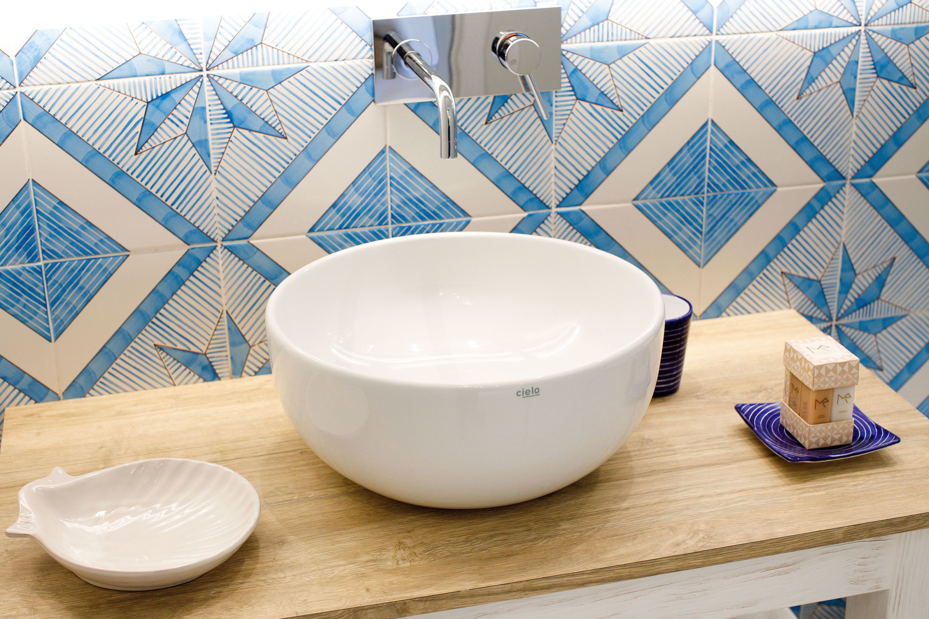 Ein Badezimmer mit einem großen weißen Waschbecken, einer Holzauszug und einer Wand mit blau-weißen Fliesen.