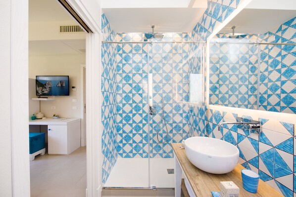 A bathroom with a shower, a sink, and a mirror. There is a TV in the adjacent room. - Melrose Sorrento (Sorrento)