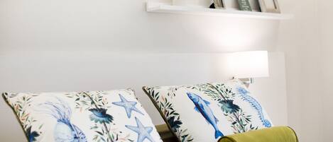 Ein Zimmer mit einem Bett, zwei Zierkissen, einem Nachttisch, einer Lampe und einem Regal mit Dekoration.