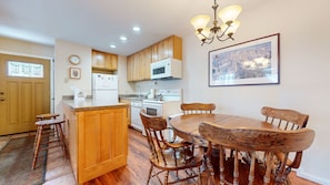 A kitchen with wooden cabinets, a dining table with chairs, a refrigerator, a microwave, and a chandelier. - San Sierra 10 Updated Condo, with Complex Jacuzzi, Short Walk to The Village by RedAwning (Mammoth Lakes)