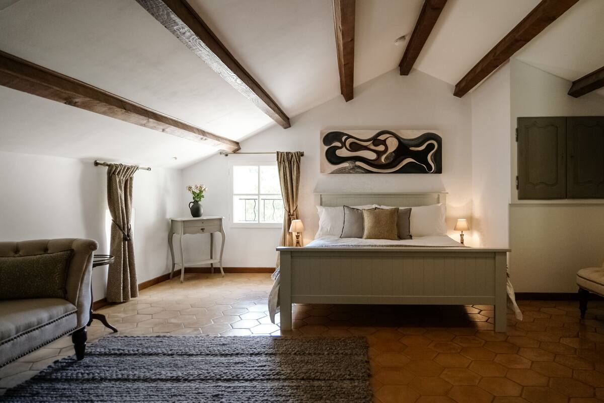 Un dormitorio con una cama, una silla, una mesita y una ventana.