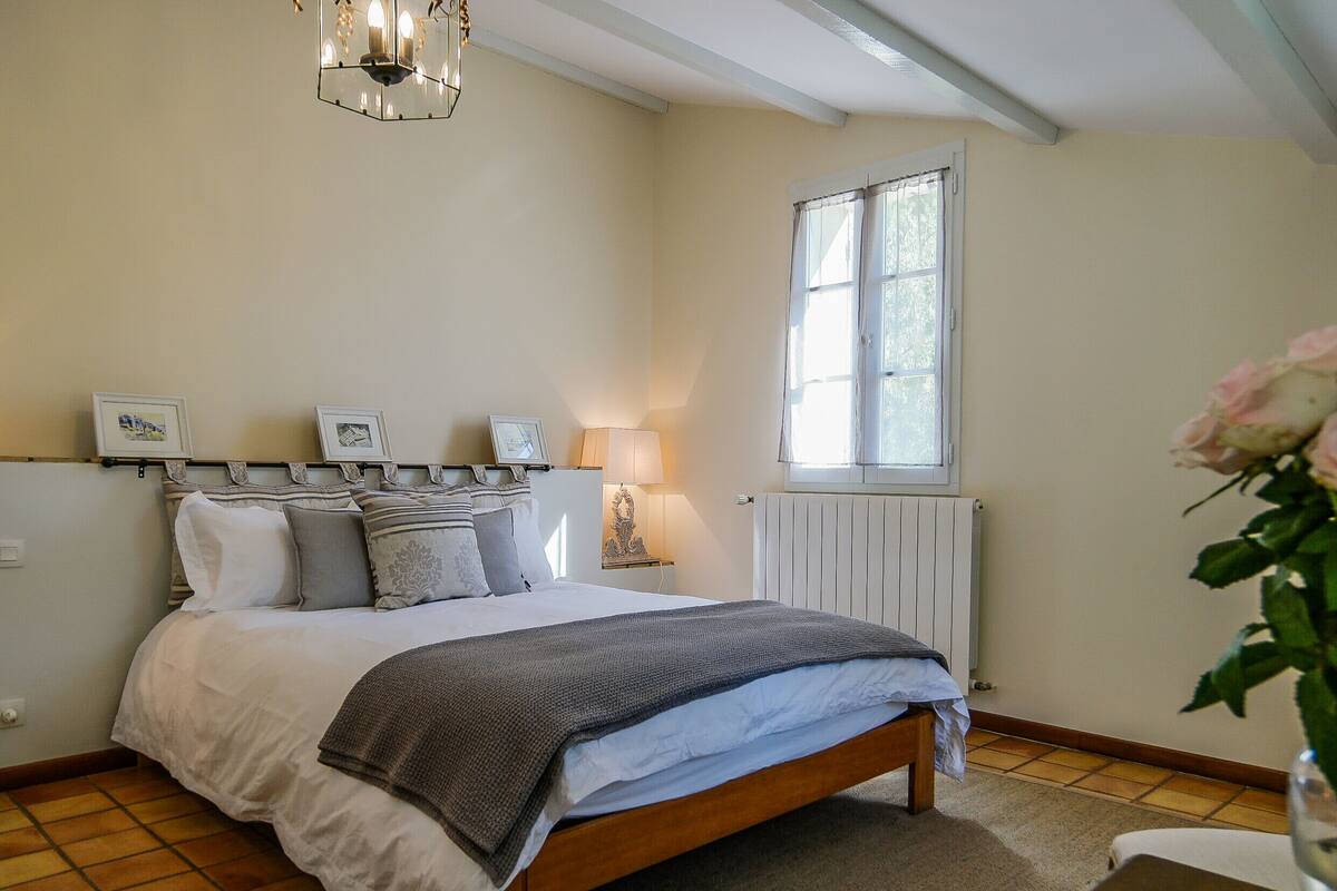 Un dormitorio con cama, lámparas de noche, una ventana y un jarrón con flores.