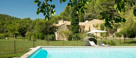 A swimming pool with a stone border, surrounded by a grassy area and a black fence.
