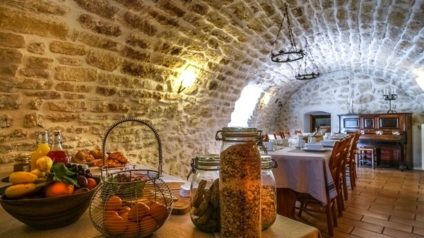 Een rustieke kamer met stenen muren, een lange eettafel gedekt met diverse soorten eten en potten.