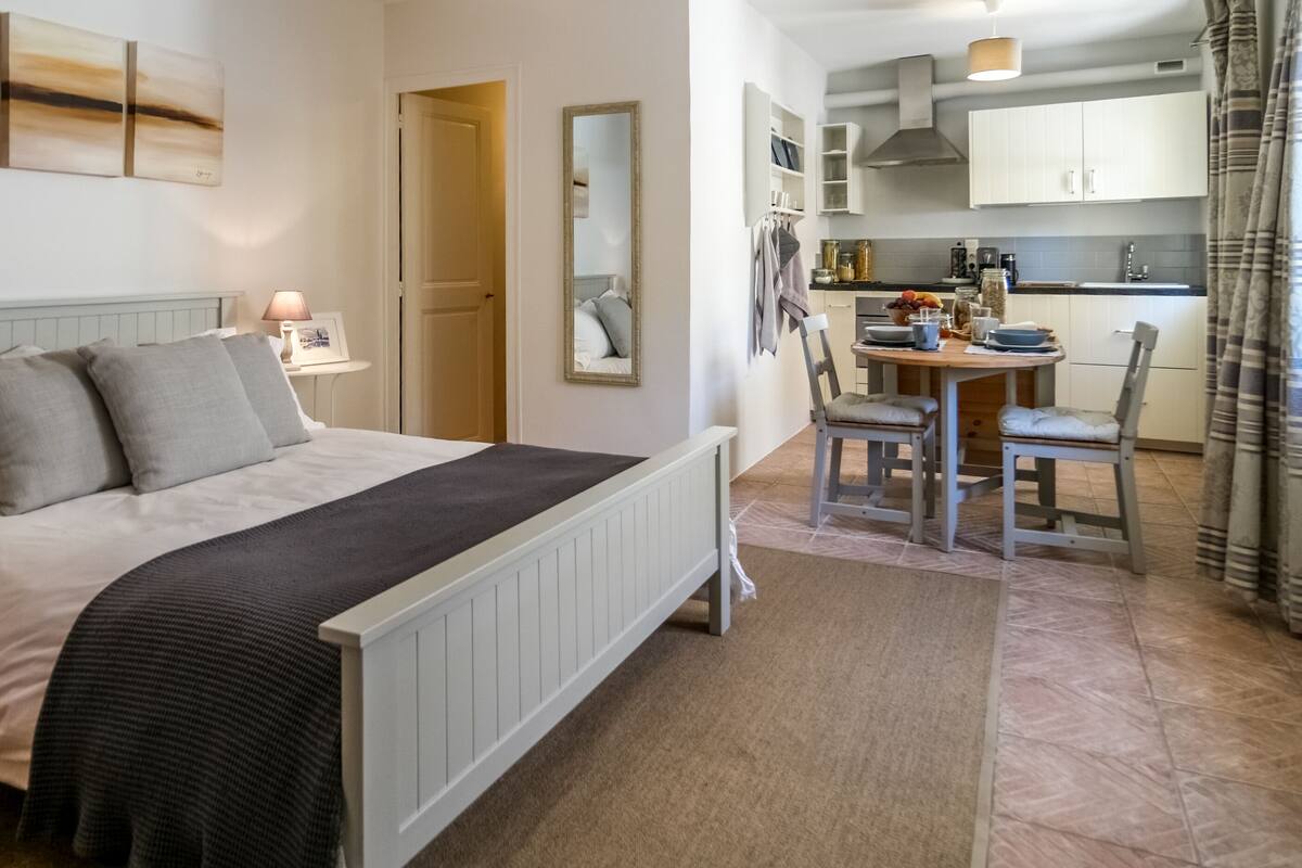 Un dormitorio con cama, mesita de noche, lámpara y vista a la cocina.