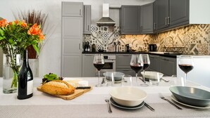 Een moderne keuken met grijze kastjes, een decoratieve spatwand, en een eettafel gedekt met brood, wijnglazen en een vaas met bloemen.