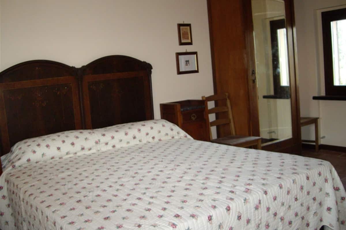 A bedroom with a wooden bed frame, a bedside table, a chair, and a mirror.