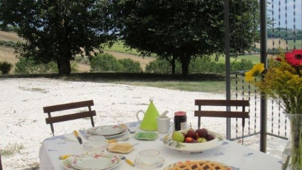 An outdoor dining table set with plates, cutlery, a teapot, a pitcher, a bowl of fruit, and a pie. - La Quercia del Saggio (Senigallia)