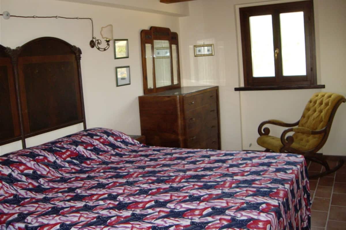 A bedroom with a bed, dresser, chair, and a window.