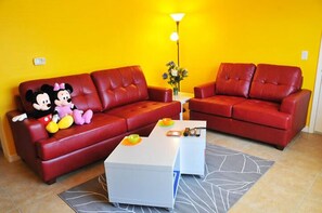A red leather sofa with two plush toys, a white coffee table, and a floor lamp in a room with yellow walls. - Sun Lake #3 - 3 Bed 3 Baths Condo (Kissimmee)