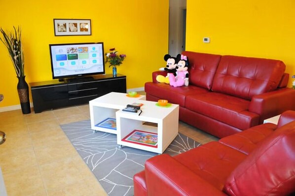 A living room with a red sofa, a white coffee table, and a flat-screen TV. - Sun Lake #3 - 3 Bed 3 Baths Condo (Kissimmee)