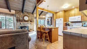 A cozy living room with a stone fireplace, wooden chairs, and a large window overlooking a forest. - Discovery 4 108 Great Complex Amenities, Close to Canyon Lodge by RedAwning (Mammoth Lakes)